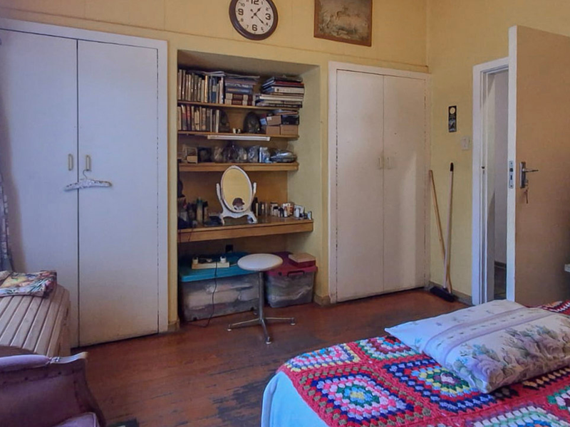 A bedroom featuring built-in cupboards, integrated shelving, and timber flooring, offering potential for modernization and cosmetic updates.
