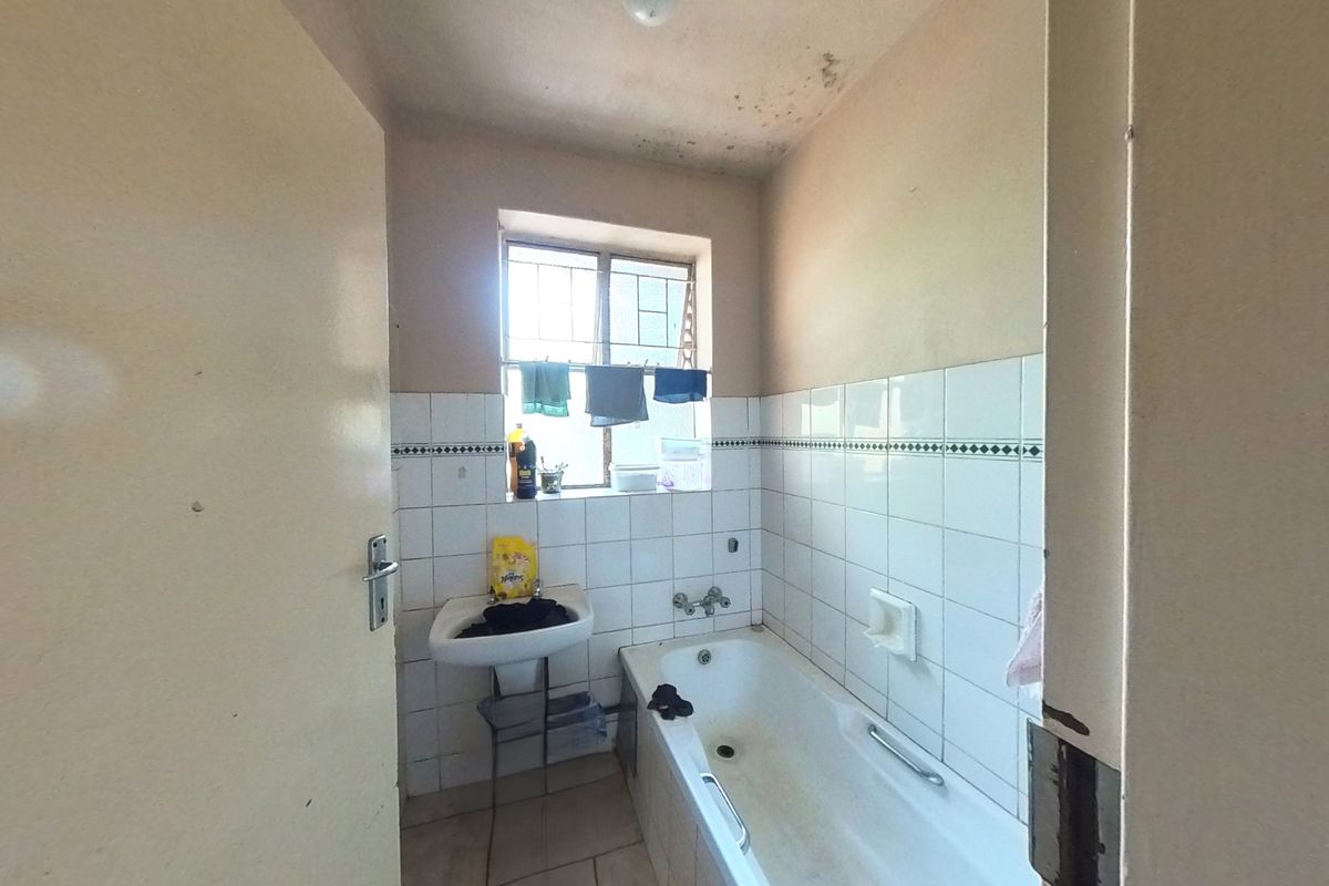 A dated bathroom featuring a bathtub, wall-mounted basin, and tiled walls, requiring cosmetic updates and repairs to the ceiling and door frame.