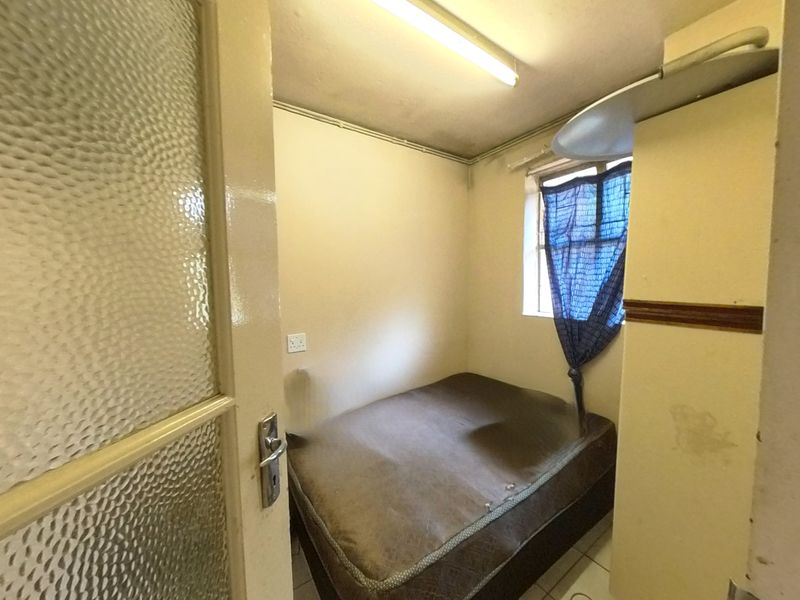 A compact bedroom featuring tiled flooring, a textured glass door, and a fluorescent light fixture, requiring cosmetic updates to the walls and ceiling.