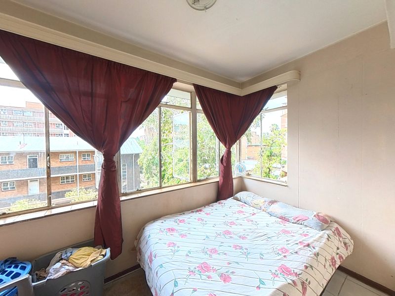 A bedroom featuring large corner windows that provide ample natural light, with tiled flooring and neutral wall finishes.