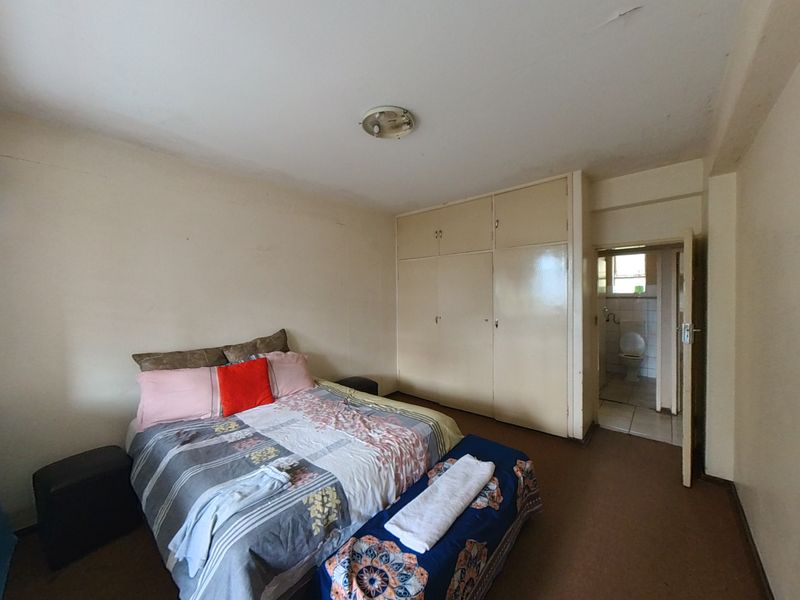 Bedroom featuring built-in cupboards and direct access to an en-suite bathroom, offering a functional layout with potential for cosmetic updates.