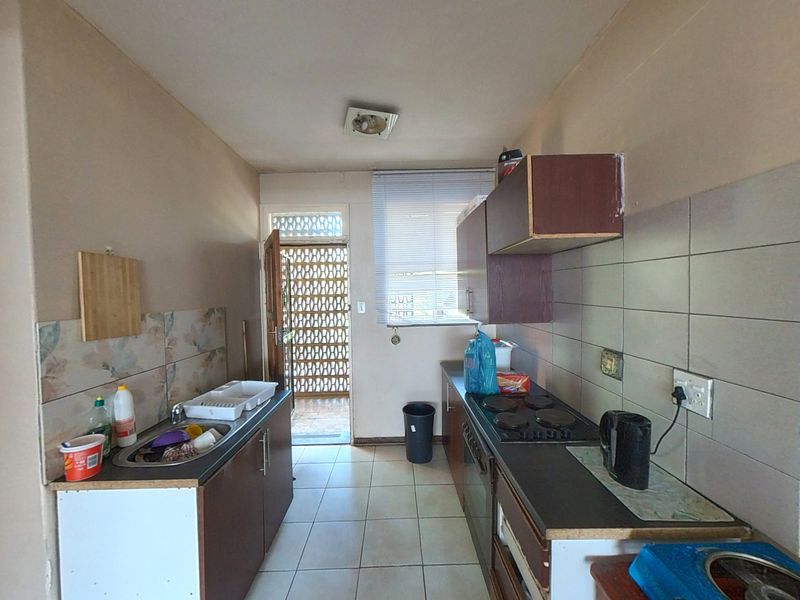 A functional galley-style kitchen featuring built-in cabinetry, an electric hob, oven, and tiled flooring, offering potential for modernization and aesthetic updates.