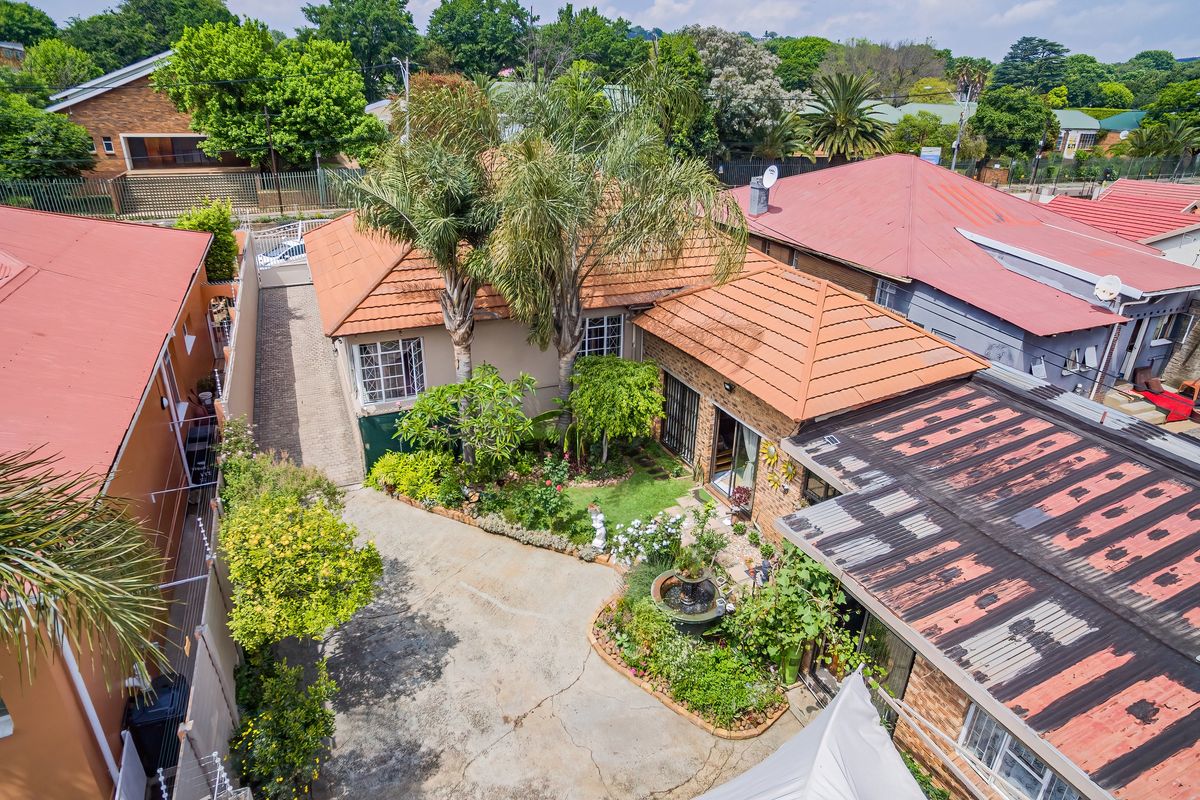 Aerial view of the property showing the tiled roof, paved driveway, landscaped garden with a fountain, and surrounding residential neighborhood.