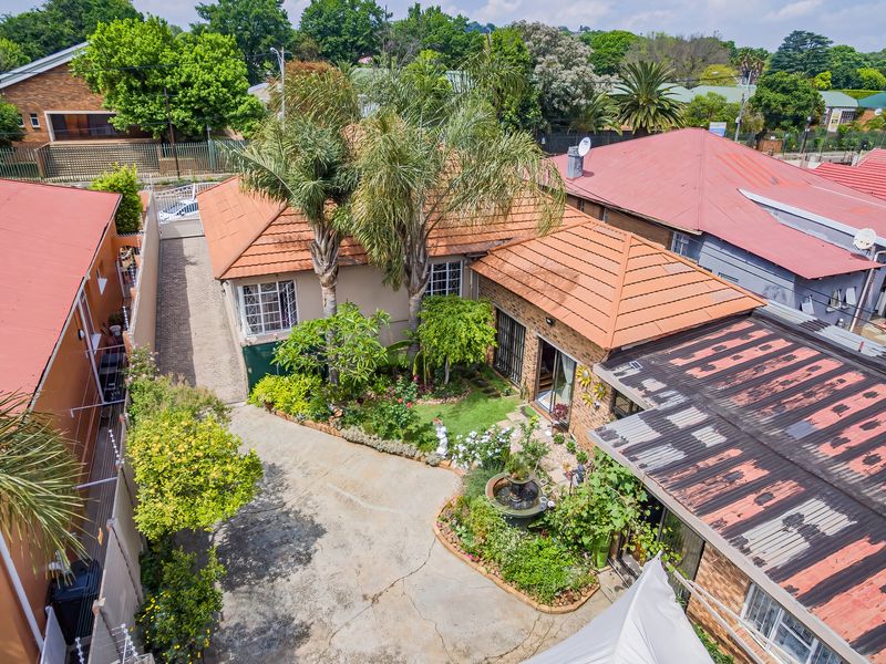 Aerial view of the property showing the tiled roof, paved driveway, landscaped garden with a fountain, and surrounding residential neighborhood.