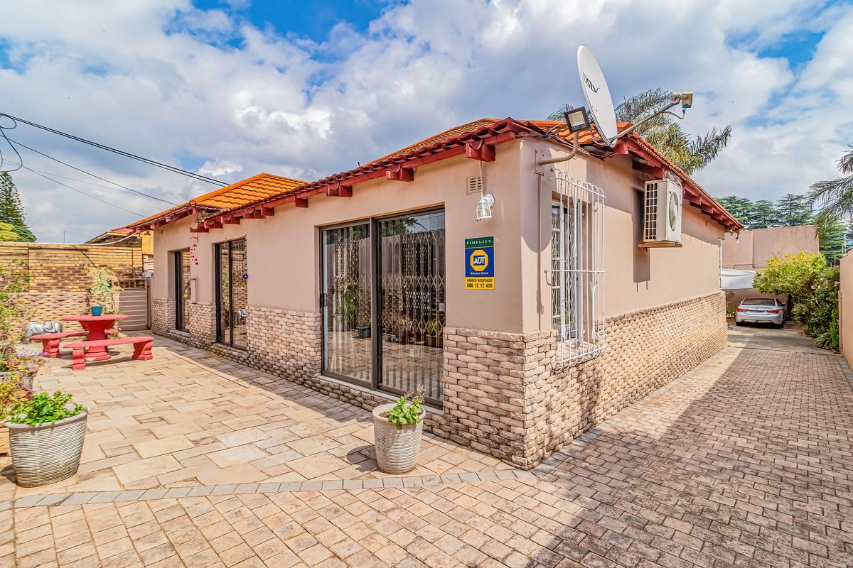 Rear exterior view featuring a paved patio area, stone-clad facade, sliding glass doors with security gates, and an installed air conditioning unit.