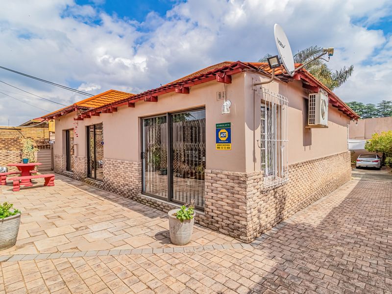 Rear exterior view featuring a paved patio area, stone-clad facade, sliding glass doors with security gates, and an installed air conditioning unit.