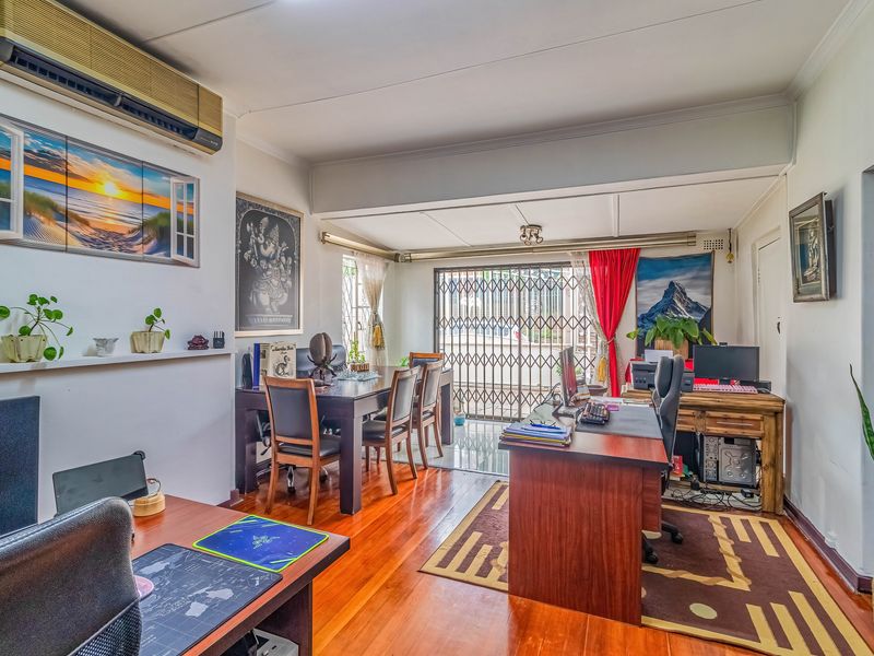 A spacious living area featuring polished hardwood flooring, a wall-mounted air conditioning unit, and a secure sliding glass door leading to the exterior.