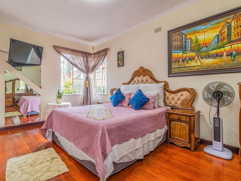 A bedroom featuring polished hardwood flooring, a large wall-mounted mirror, and windows fitted with security bars.