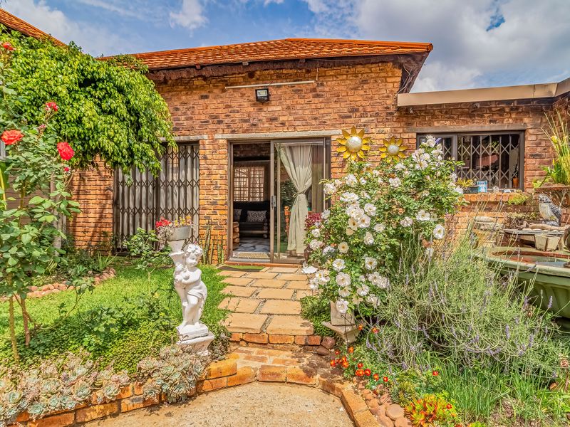A charming rear exterior view featuring a face brick facade, tiled roof, and a well-maintained garden with a stone pathway and water feature.