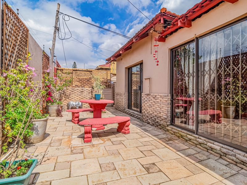 A paved outdoor patio area featuring stone cladding, sliding glass doors with security gates, and a tiled roof structure.