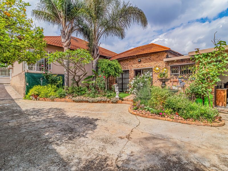 Front exterior view of a brick house featuring a paved driveway, established garden beds, and a tiled roof.
