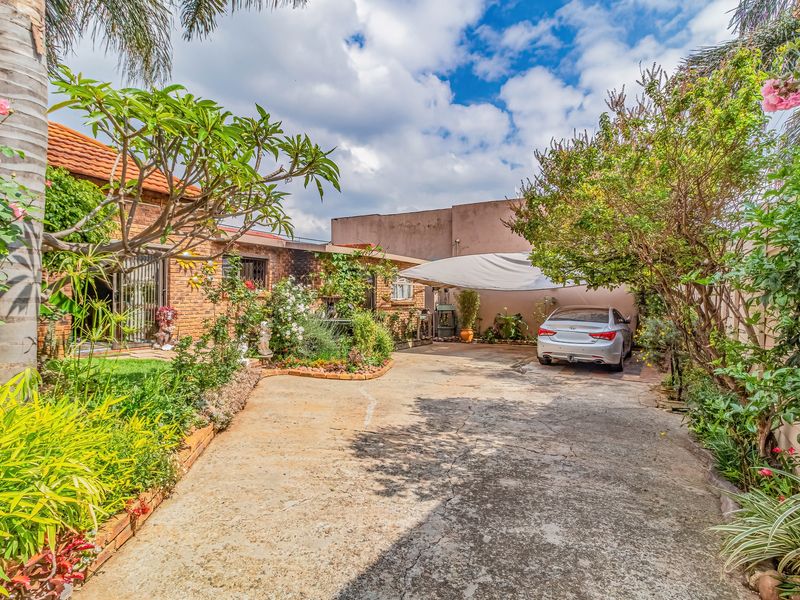 Front exterior view featuring a concrete driveway, established garden, brick facade, and a covered carport area.
