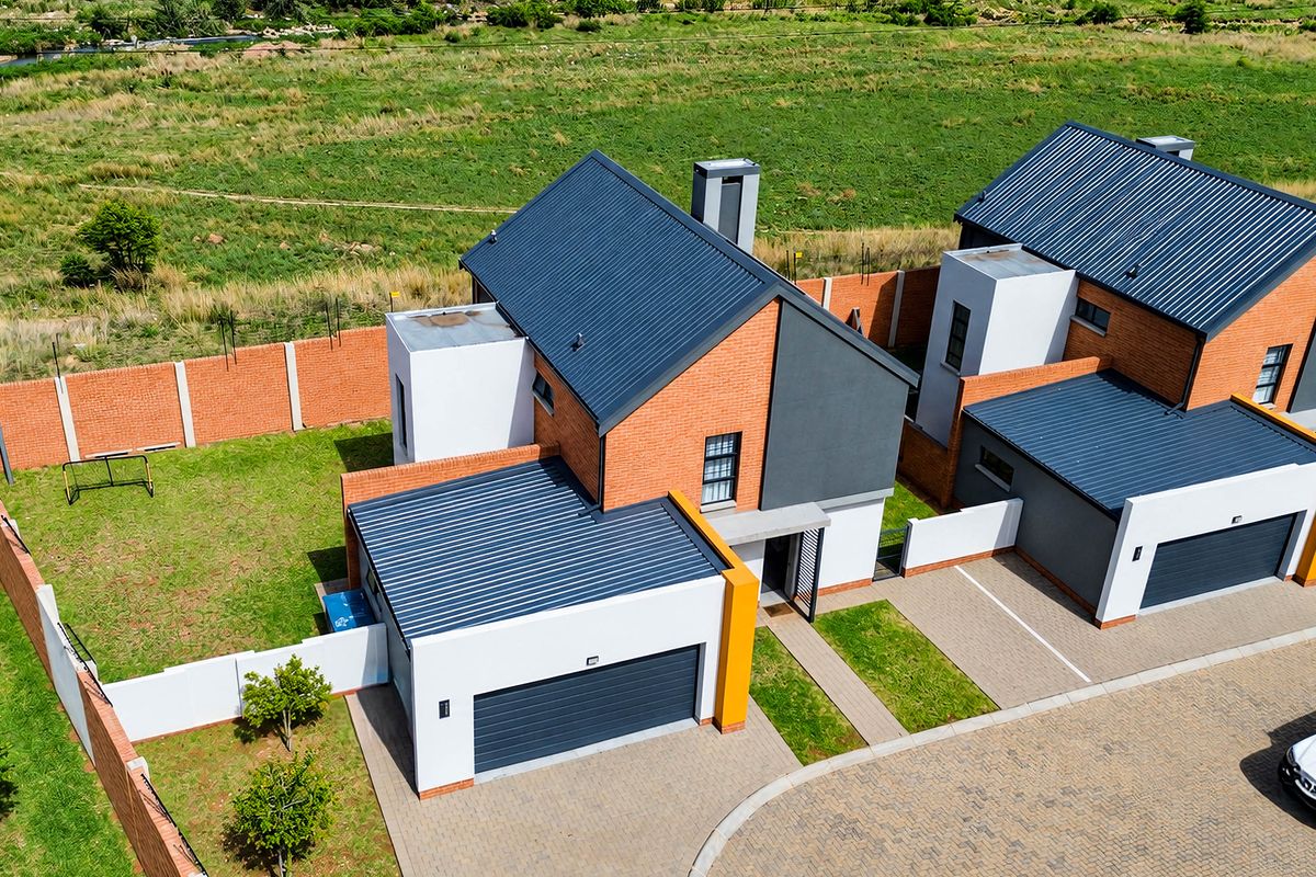 Aerial view of a modern townhouse complex featuring brick and rendered facades, corrugated metal roofing, private gardens, and paved driveway access.