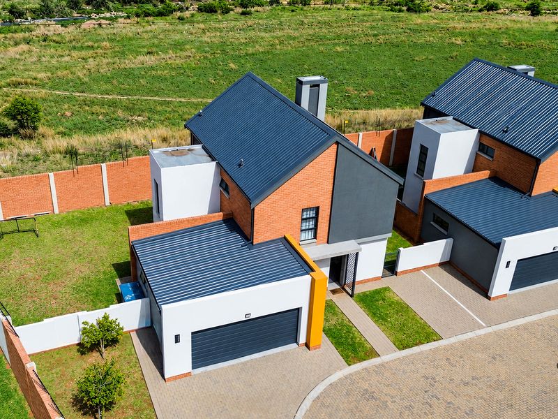 Aerial view of a modern townhouse complex featuring brick and rendered facades, corrugated metal roofing, private gardens, and paved driveway access.