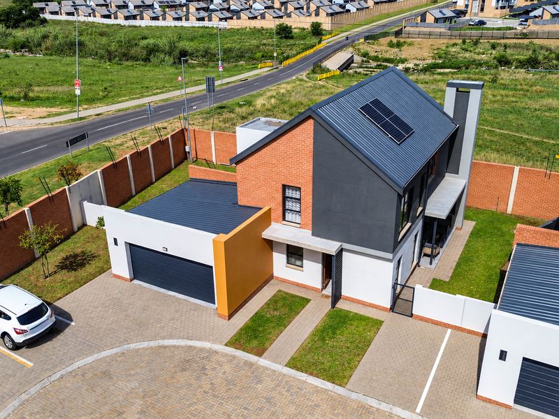 Aerial view of a modern townhouse featuring a brick and rendered facade, metal roof with solar panels, paved driveway, and enclosed perimeter wall.