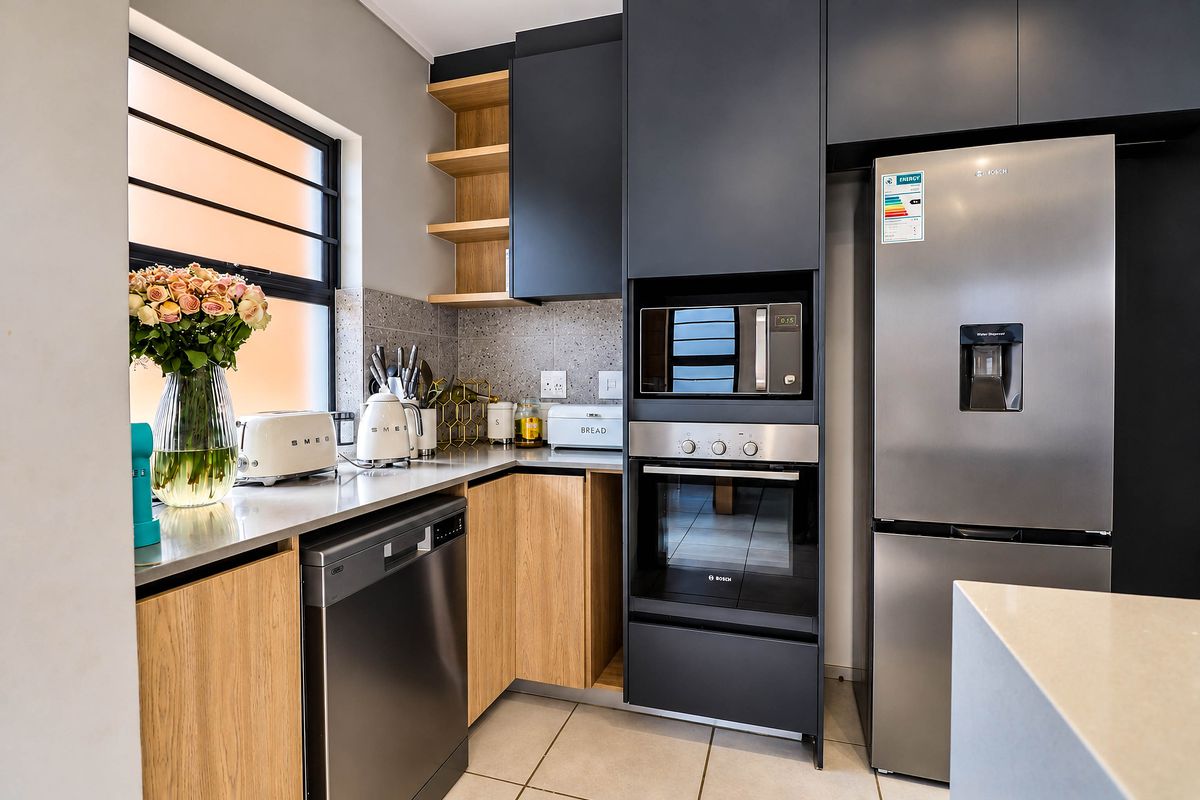 Modern kitchen featuring sleek dark cabinetry, light wood accents, stone countertops, and high-quality built-in appliances including an oven, microwave, and dishwasher.
