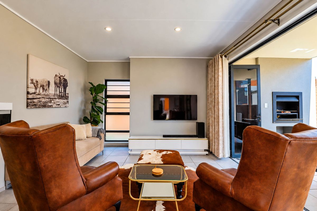 A well-maintained living room featuring tiled floors, recessed lighting, and seamless access to an outdoor patio area with a built-in braai.