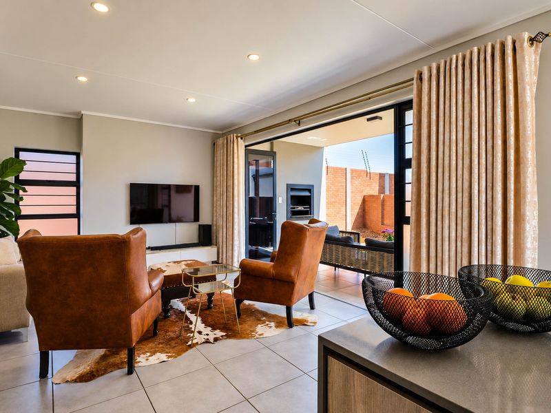 Modern open-plan living area featuring tiled floors, recessed lighting, and seamless flow to a covered patio through large sliding glass doors.