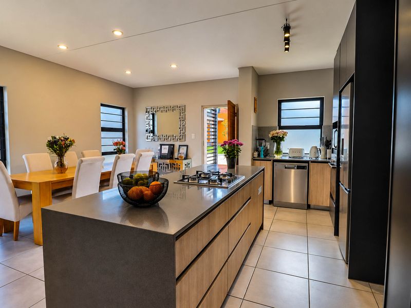 Modern open-plan kitchen and dining area featuring a central island with gas cooktop, sleek cabinetry, and tiled flooring throughout.