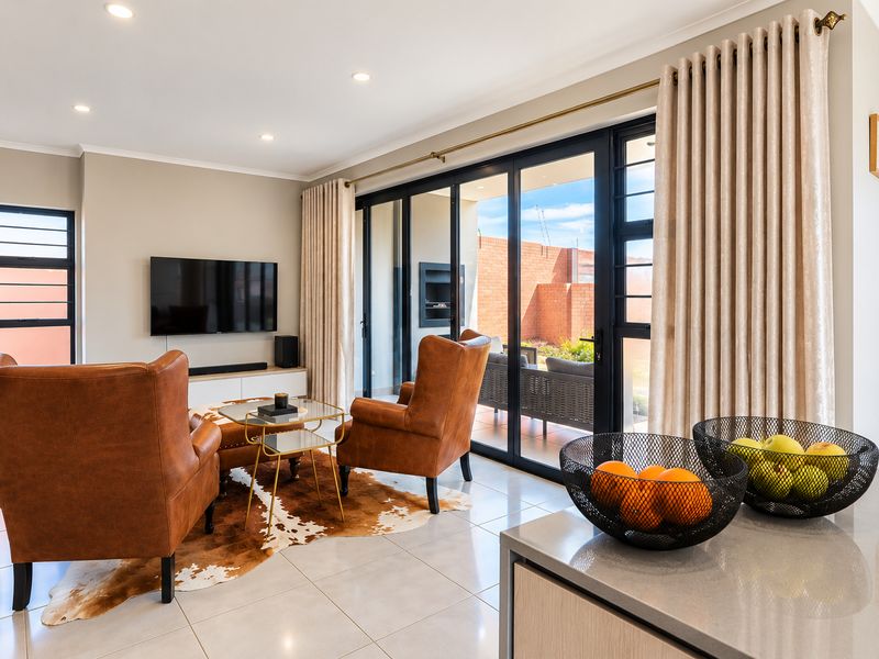 Modern open-plan living area featuring tiled floors, recessed lighting, and large black aluminium sliding doors providing seamless access to the outdoor patio.
