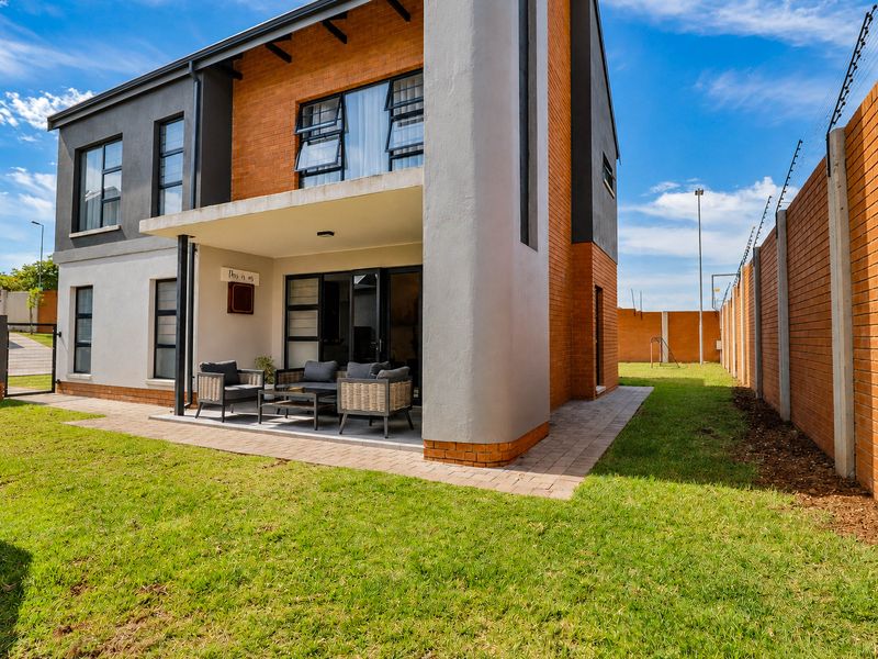 Rear view of a modern townhouse featuring a covered patio, brick and rendered facade, and a private garden enclosed by a perimeter wall.