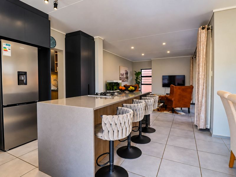 Modern open-plan living area featuring a sleek kitchen island with a gas hob, stone countertops, and contemporary cabinetry, seamlessly flowing into the lounge space.