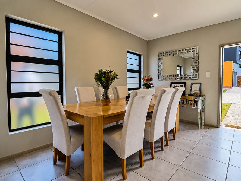 A bright and well-maintained dining room featuring neutral tiled flooring, modern aluminium windows, and recessed lighting, with direct access to the exterior.