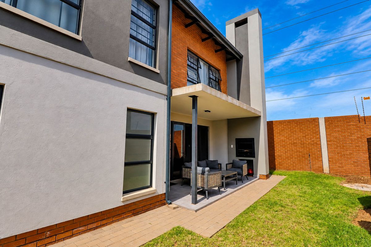 Rear view of the townhouse featuring a covered patio with a built-in braai, paved walkway, and a private garden area with brick boundary walls.