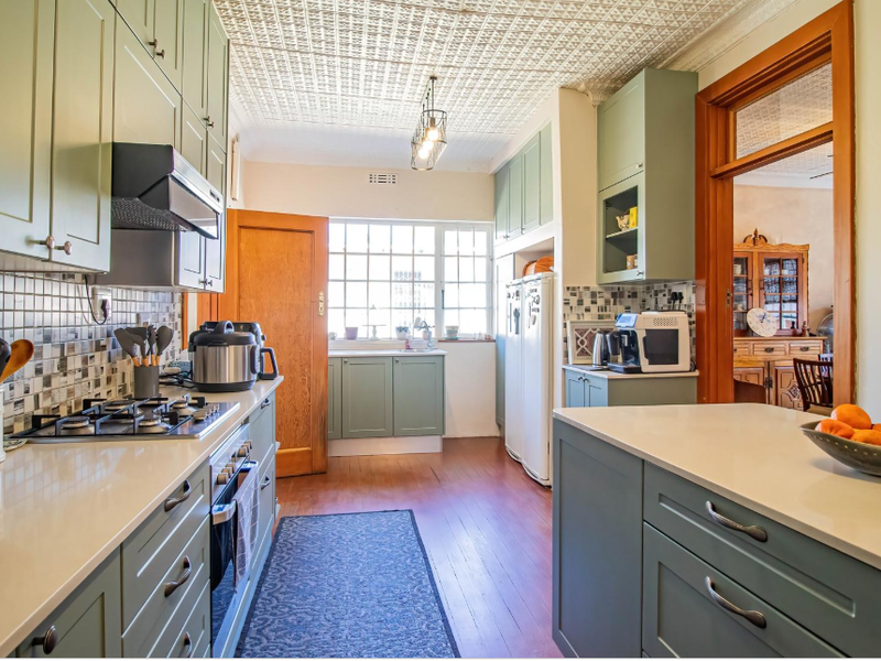 A well-appointed kitchen featuring sage green shaker-style cabinetry, quartz countertops, a gas hob, and a distinctive pressed metal ceiling with hardwood flooring.