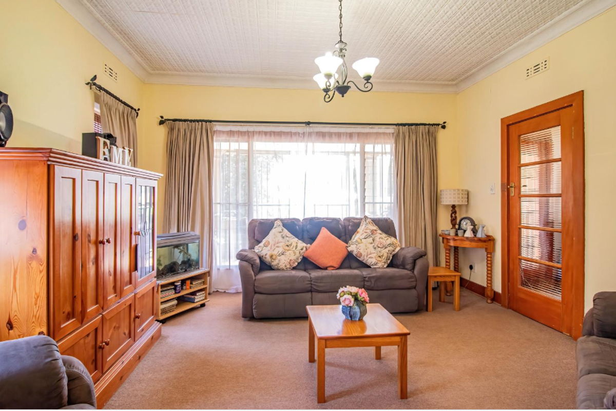 A comfortable living room featuring a classic pressed metal ceiling, carpeted flooring, and a timber-framed glass door leading to adjacent spaces.