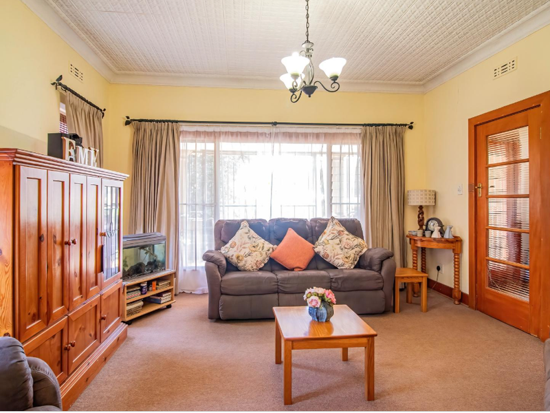 A comfortable living room featuring a classic pressed metal ceiling, carpeted flooring, and a timber-framed glass door leading to adjacent spaces.