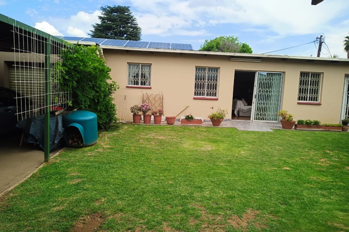 Rear view of the property featuring a well-maintained lawn, solar panels on the roof, and a covered carport area.