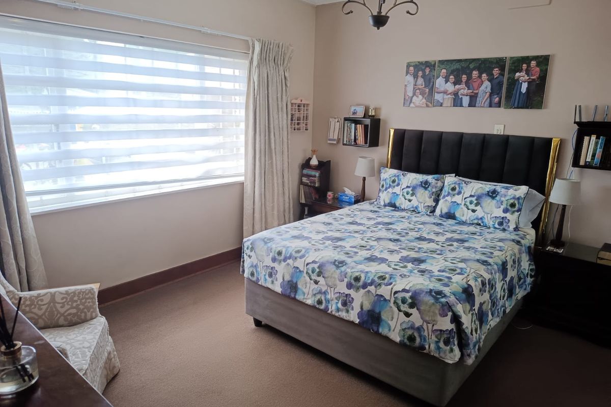 A well-maintained bedroom featuring neutral wall tones, carpeted flooring, and a large window providing natural light.