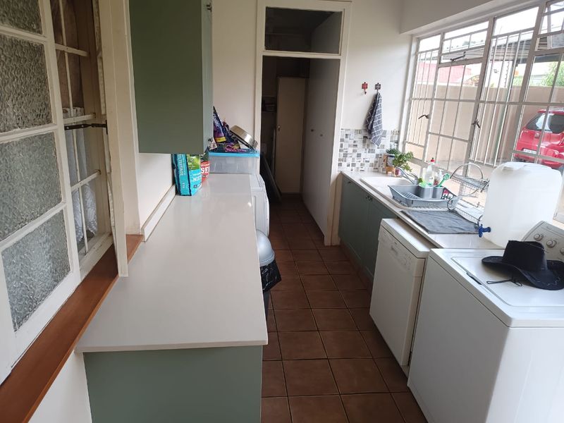 A functional laundry room featuring built-in cabinetry, laminate countertops, a double sink, and tiled flooring with large steel-framed windows.