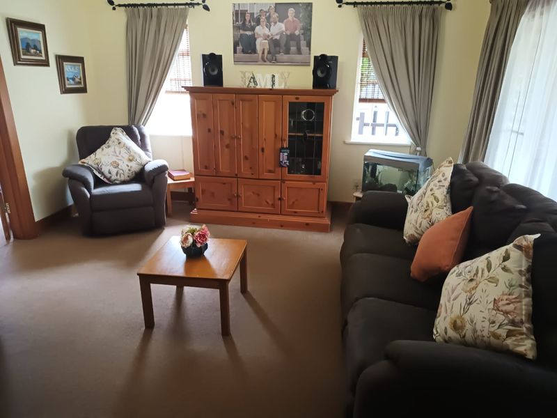 A comfortable living room featuring neutral walls, carpeted flooring, and dual windows with curtains, providing a functional and inviting space.