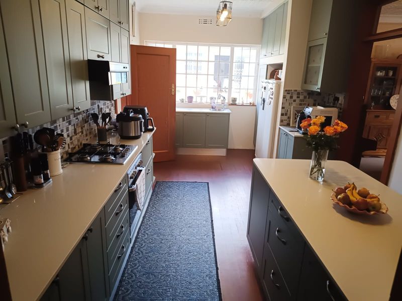 A well-maintained kitchen featuring sage green cabinetry, stone countertops, a central island, and a gas hob with a mosaic tile backsplash.