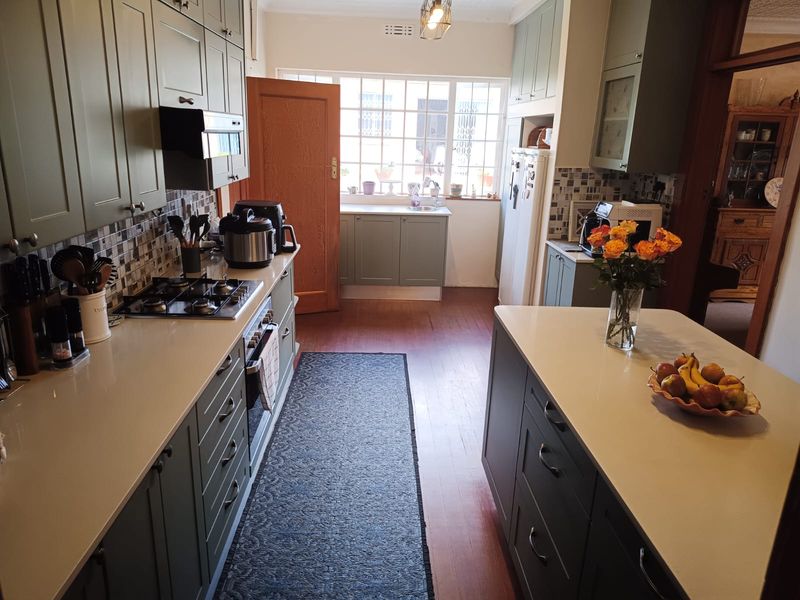 A well-appointed kitchen featuring sage green cabinetry, stone countertops, a gas hob, and a central island, offering a functional and stylish cooking space.