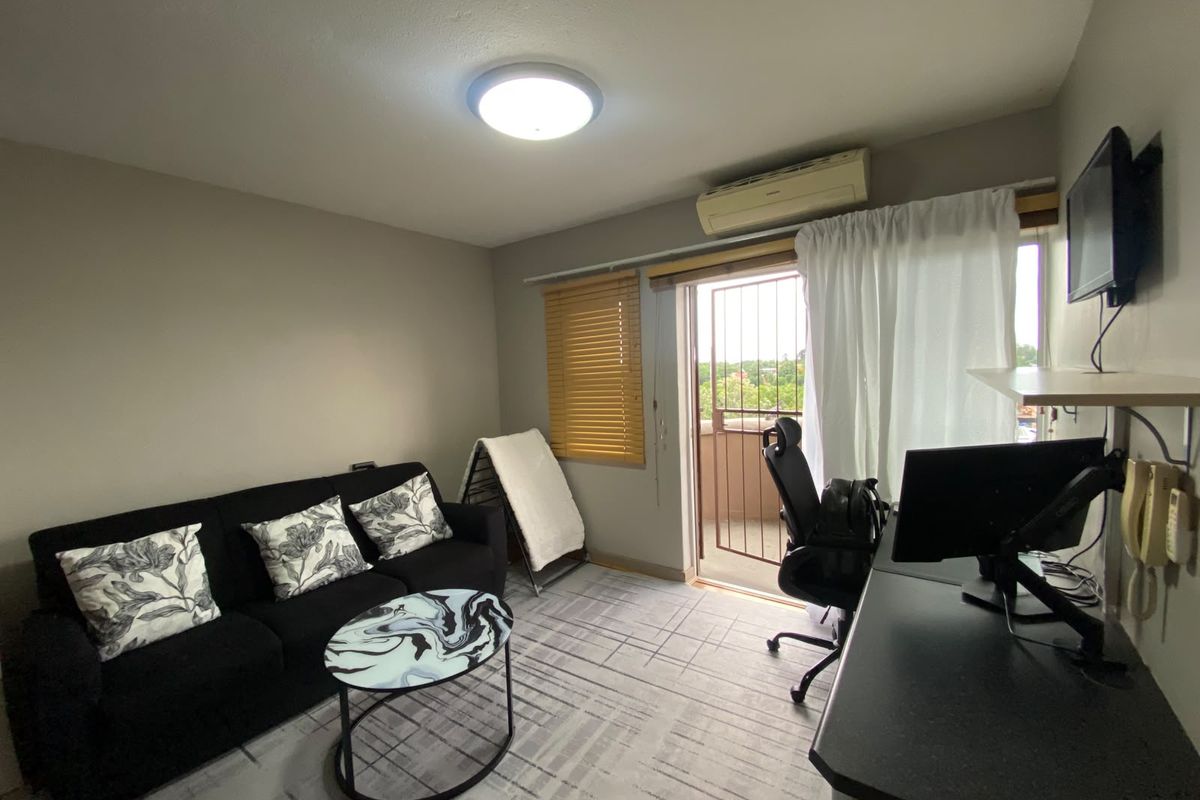A functional living area featuring a split-system air conditioner, security gate access to a balcony, and neutral finishes.