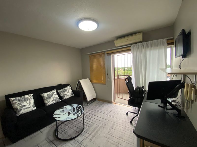 A functional living area featuring a split-system air conditioner, security gate access to a balcony, and neutral finishes.