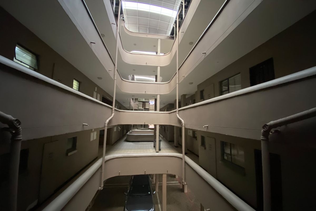 An open-air central atrium or courtyard within an apartment complex, featuring multi-level walkways, balustrades, and a skylight roof.