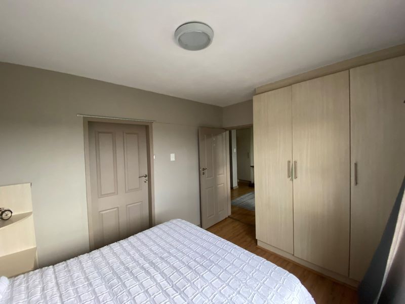 A well-maintained bedroom featuring light wood-tone built-in cupboards, laminate flooring, and neutral wall finishes, offering a clean and functional living space.