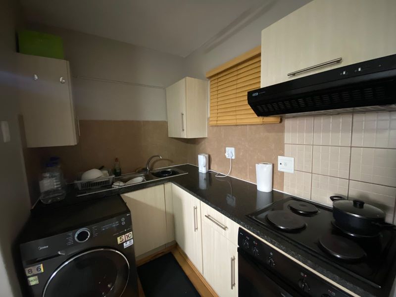 Compact kitchen featuring light-toned cabinetry, dark granite countertops, a built-in electric hob with extractor fan, and tiled backsplash.