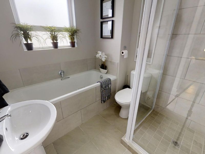 A modern, well-maintained bathroom featuring a built-in bathtub, a separate glass-enclosed shower, a pedestal basin, and neutral floor-to-ceiling tiling.