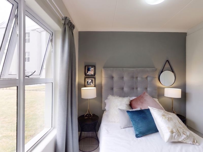 A well-maintained bedroom featuring a built-in wardrobe, neutral grey accent wall, and a large casement window providing natural light.