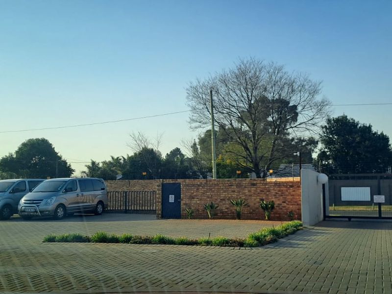 Front entrance view of the townhouse complex featuring a paved driveway, secure gated access, and brick boundary walling.
