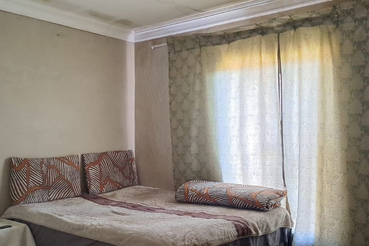 A bedroom featuring a window with curtain rails and visible water staining on the ceiling.