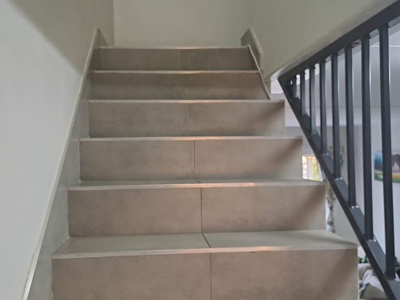 A staircase featuring tiled steps, a sturdy metal handrail, and a matching metal balustrade, providing a clean and functional transition between levels.