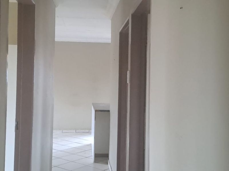 A view through a residential hallway leading into an open plan living area with tiled flooring and neutral wall finishes.