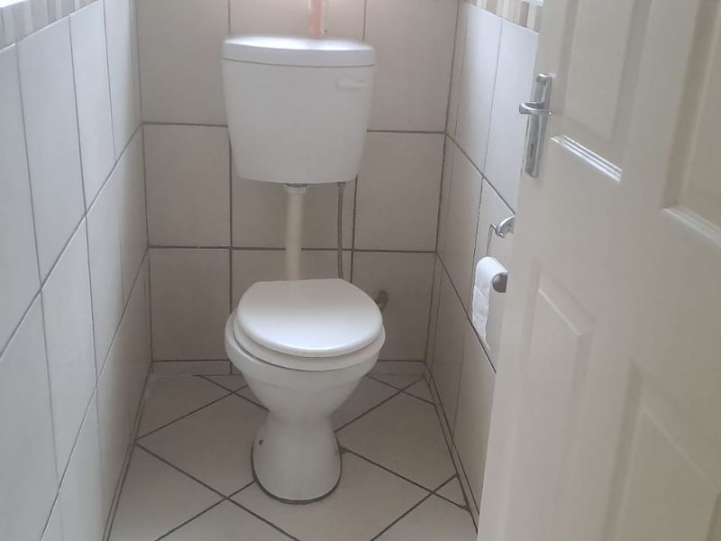 A compact, functional guest toilet featuring neutral ceramic wall and floor tiling.