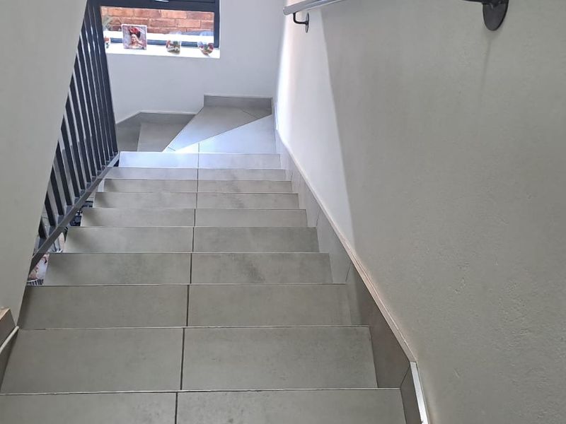 A clean, modern staircase featuring neutral floor tiles, a sturdy metal handrail, and a matching metal balustrade.